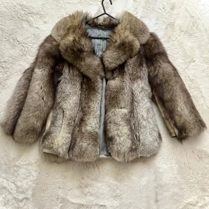 Brun falsk pälsjacka - Säljer en lyxig brun pälsjacka med en mjuk och fluffig känsla. Jackan har en klassisk design med långa ärmar och en elegant krage. Perfekt för att hålla sig varm och stilren under kyliga dagar.