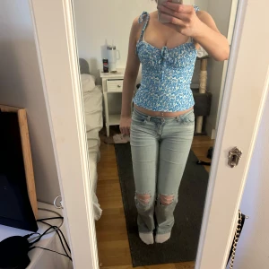 Blå blommig korsettopp - Säljer en söt blå korsettopp med blommigt mönster och knytband vid axlarna. Toppen har en smickrande passform och en liten rosett framtill. Perfekt för sommarens alla tillfällen!