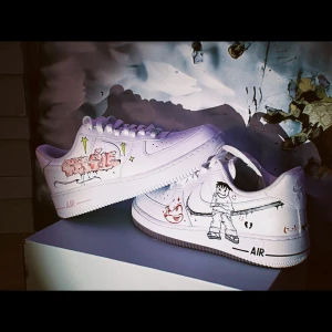 Custom Nike Air Force med konstnärliga motiv - Unika Nike Air Force sneakers med handmålade motiv. Ena skon har en tecknad figur och text, medan den andra pryds av en blå fjäril och stjärnor. Perfekt för den som vill sticka ut med sina skor.