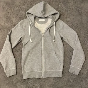 Grå hoodie från Pier One - Säljer en stilren grå hoodie från Pier One. Den har en dragkedja framtill och justerbara snören i huvan. Hör av dig direkt vid frågor!