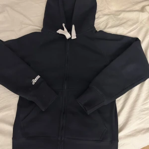 Mörkblå hoodie från Russe merch - Säljer en mörkblå kofta från Russemerch med dragkedja. Den har en broderad logga på ärmen. Perfekt för en avslappnad stil.