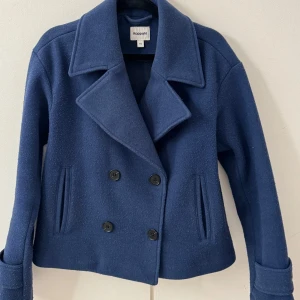 Blå kappa från Kappahl - Snygg blå kappa från Kappahl med dubbelknäppning och bred krage. Jackan har långa ärmar och två framfickor. Perfekt för våren! Nypris 1100kr