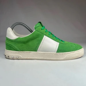 Gröna sneakers från Valentino - Snygga gröna sneakers från Valentino med vita detaljer och snörning. Skorna har en stilren design med en kontrasterande vit panel på sidan och små nitar på sulan. Perfekta för en trendig look. Box medföljer inte men extra snören medföljer. Ny pris 6510kr