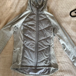 Hybridjacka - Säljer en grå sportjacka/hybridjacka från H&M med dragkedja och huva. Jackan har en quiltad design på framsidan och baksidan. Perfekt för träning eller en aktiv vardag. Sitter åt så ger superfin passform😍