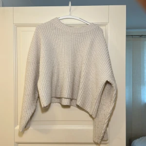 Beige stickad tröja från H&M - Säljer en mysig beige stickad tröja från H&M. Tröjan har en croppad design med långa ärmar och en ribbad struktur. Perfekt för kyliga dagar!
