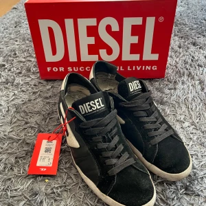Diesel skor - Snygga svarta sneakers från Diesel med vit sula och röd undersida. Skorna har snörning och en tydlig Diesel-logga på plösen. Perfekta för en stilren look.