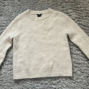 Beige stickad tröja från Lindex - Mysig beige stickad tröja från Lindex. Perfekt för kyliga dagar med sin klassiska design och ribbade detaljer vid ärmslut och nederkant. Enkelt att matcha med olika outfits. Köpt för 600kr