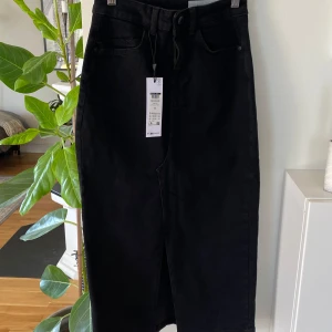 Svart jeanskjol från Noisy May! XS! Prislappar kvar! - Snygg svart lång  jeanskjol från Noisy May med en klassisk design. Kjolen har en slits framtill och stängs med dragkedja och knapp. Perfekt för en stilren look.prislappar kvar! Den är helsvart inga skuggor osv som på bilden. Fler bilder, skriv! 🌸