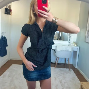 Svart prickig blus med knytband - Otroligt fin och eftertraktad svart ”skjorta”/blus med vita prickar och korta ärmar. Blusen har knappar framtill midjan och ett knytband i midjan för en smickrande passform. Såå trendig och svår att få tag på💕 från ”french collection” i storlek 38, men sitter som en XS/S