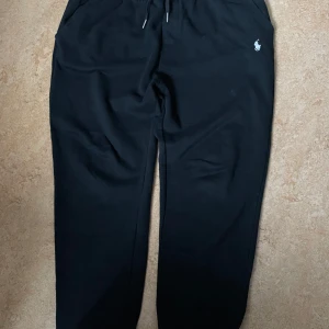 Svarta mjukisbyxor från Polo Ralph Lauren - Snygga svarta mjukisbyxor från Polo Ralph Lauren med det klassiska broderade logotypen i vitt. Byxorna har en bekväm passform med snörning i midjan för justerbarhet. Passar även perfekt i storlek L.