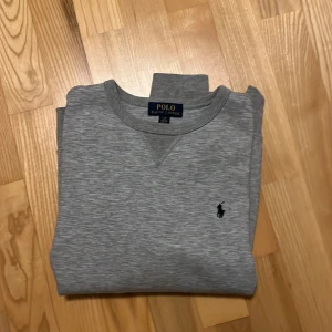 Grå tröja från Polo Ralph Lauren - Säljer en stilren grå tröja från Polo Ralph Lauren med rund hals. Tröjan har långa ärmar och är perfekt för en avslappnad look. Tröjan har endast används enstaka gånger och är perfekt skick.