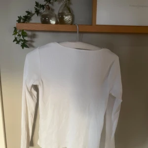 Vit ribbad topp från Pieces - Säljer en stilren vit ribbad topp från Pieces med v-ringning och långa ärmar. Perfekt för en enkel och snygg look. Toppen har en diskret rynkning framtill som ger en fin detalj. Tröjan har bara används 1 gång