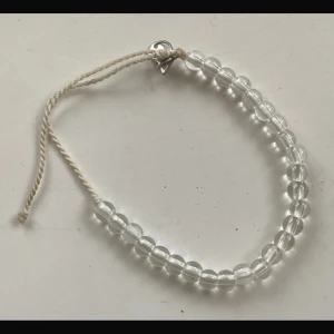 Transparent armband med pärlor - Snyggt armband med transparenta pärlor och en justerbar vit snörning. Perfekt för att ge en subtil touch till din stil. Armbandet har en liten silverfärgad detalj som ger det en extra charm.