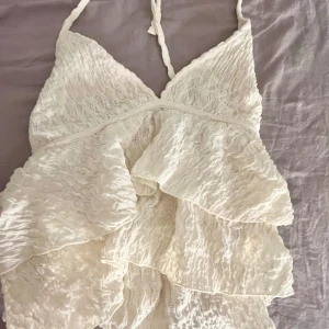 Vit spetslinne med volanger - Säljer ett vackert vitt linne med spets och volanger från gina tricot. Toppen har smala axelband och en v-ringad design. Perfekt för sommarens alla tillfällen. 💫