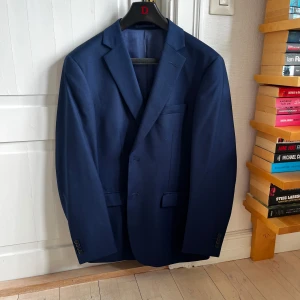 Mörkblå kavaj från Dressmann - Snygg mörkblå kavaj från Dressmann i klassisk design. Kavajen har två knappar framtill och en stilren passform. Perfekt för både formella och semi-formella tillfällen.