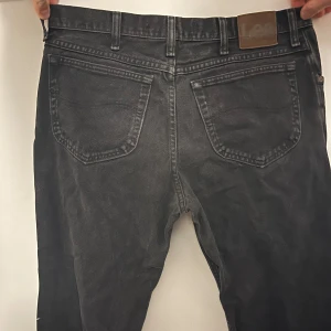 Svarta jeans från Lee - Snygga svart gråa jeans från Lee med klassisk femficksdesign och knappgylf. Perfekta för en stilren look. W 36, L 30, regular fit