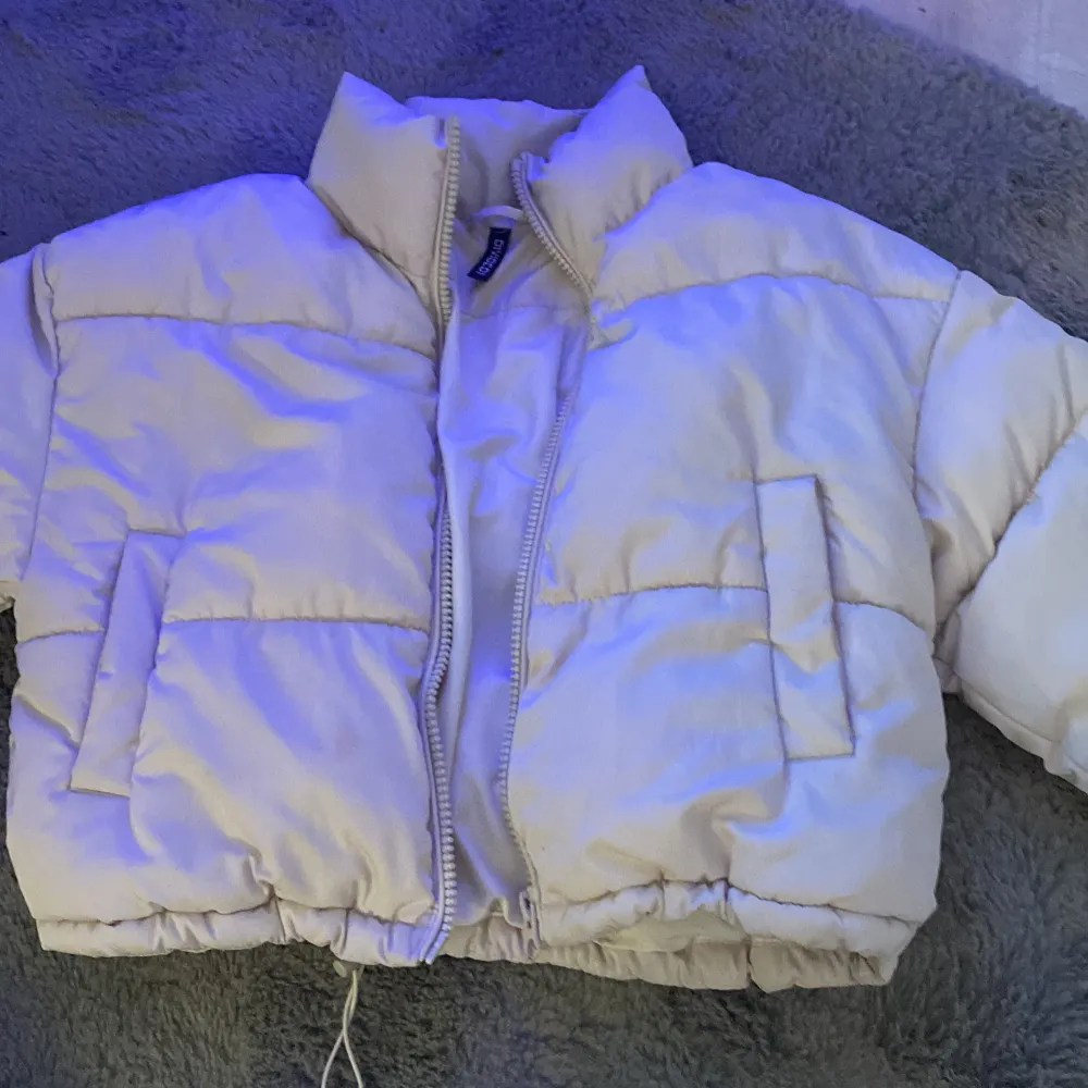 Säljer en snygg vit pufferjacka från Divided. Jackan har en dragkedja framtill och är perfekt för kyligare dagar. Den har en hög krage och två praktiska fickor på sidorna. Perfekt för att hålla värmen med stil!. Takit.