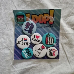 K-Pop Button Badges - Säljer ett set med K-Pop-inspirerade knappmärken. Innehåller olika designs med texter som 'I ♥ K-Pop' och 'Love is not over'. Perfekt för att dekorera väskor eller kläder och visa din kärlek för K-Pop! 8 kr styck, 64 kr för alla (hela paketet)