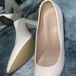 Ljusrosa pumps med klack - Säljer ett par ljusrosa pumps med rund tå och klack. Skorna har en stilren design och är tillverkade i syntetmaterial med en slät yta. Perfekta för dig som vill ha en klassisk och enkel sko med feminin touch.