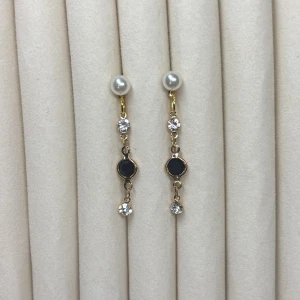 Guldiga örhängen med pärlor och svarta detaljer - Snygga örhängen med vit pärla upptill, gnistrande stenar och en svart rund sten i mitten. Hängande modell i guldfärgad metall som ger en elegant look.