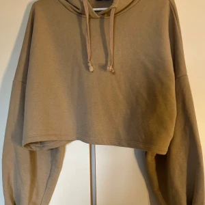 Beige croppad hoodie från Madlady - Säljer en beige croppad hoodie från Madlady i storlek S. Tröjan har huva med dragsko och långa ärmar. Perfekt för en avslappnad och trendig look.