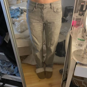 Grå raka jeans - Säljer ett par grå jeans med rak passform och klassisk femficksdesign. Byxorna har midrise midja och stängs med dragkedja och knapp. Perfekta för en avslappnad och stilren look.