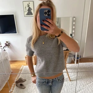 Grå stickad tröja från Zara - Säljer en stilren grå stickad tröja från Zara. Tröjan har korta ärmar och en rund halsringning, perfekt för en avslappnad look. Den är mjuk och bekväm, idealisk för både vardag och lite kyligare dagar.