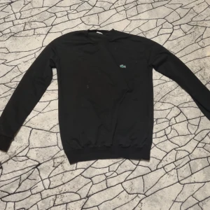 Svart sweatshirt från Lacoste - Säljer en svart sweatshirt från Lacoste med klassisk krokodillogga på bröstet. Tröjan har rund halsringning och långa ärmar. Perfekt för en stilren och enkel look.