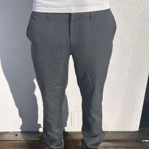 Gråa kostymbyxor från Dressmann - fräscha gråa kostymbyxor perfekta till festligare tilllfällen men även vardagliga. Skicket är fint, den ända nackdelen är att föregående ägare sprättat upp dessa längst ner (syns på bilden) varav en en rand som ska va innanför syns, detta syns inte överdrivet mycket men kan också tas bort om man syr upp byxan lite. För referens är modellen 185 cm lång ungefär. Byxorna är från Dressman och storleken är tyvärr oklar så det inte finns någon lapp. Vanligtvis har modellen storlek M i byxor.