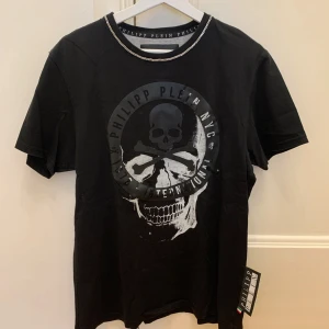 Svart t-shirt Limited edition med dödskalletryck från Philipp Plein - Svart limited edition t-shirt från Philipp Plein. Dödskalletryck på framsida samt kedjeliknande detalj runt krage ut på axlar. Dm vid intresse för fler bilder.