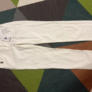 Vita slim byxor från USPA - Säljer ett par vita slim byxor från USPA med broderad logga vid fickan. Byxorna har klassisk femficksdesign och är tillverkade i ett mjukt bomullsmaterial. Perfekta för dig som gillar stilrena och fräscha plagg.