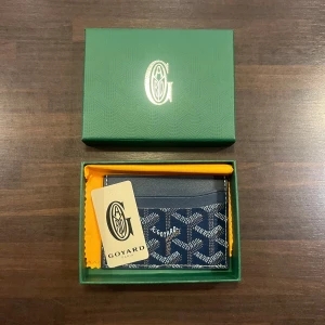 Blå Korthållare  - Exklusiv blå korthållare  med sitt fina mönster. Tillverkad i skinn med vita och beige detaljer. Kommer i boxen med certifikat och putsduk. Perfekt för att hålla ordning på dina kort med stil. Nästan aldrig använd