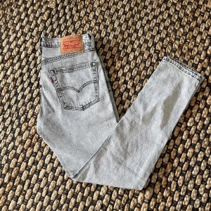 Ljusgrå Levi's jeans - Säljer ett par klassiska ljusgrå Levi's jeans med raka ben och femficksdesign. Jeansen har den ikoniska läderpatchen bak i midjan och röd Levi's-tagg på bakfickan. Perfekta för dig som gillar vintagekänsla och tidlös stil.