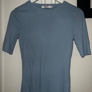 Blå ribbad topp från NA-KD - Säljer en ljusblå ribbad topp från NA-KD med korta ärmar och rund halsringning. Enkel och stilren modell som passar perfekt till både jeans och kjol. Supermjuk och stretchig i materialet.