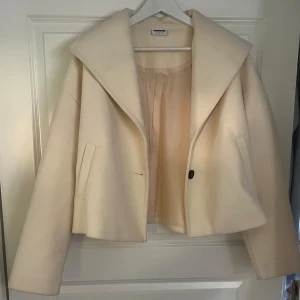 Beige kappa från Vero Moda - Säljer en stilren beige kappa från Vero Moda med bred krage och en knapp framtill. Jackan har två fickor och är croppad i modellen, vilket ger en modern look. Perfekt för dig som vill ha en snygg och enkel jacka till vardags.
