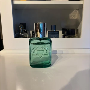 Parfums de Marly greenely  - Greenley från Parfums de Marly är en lyxig herrparfym i en grön glasflaska med silverfärgad kork. Flaskan har två upphöjda hästar och märkets logotyp på framsidan. Doften är fräsch och modern, perfekt för dig som gillar exklusiva parfymer.