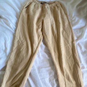 Beiga mjukisbyxor från 157 - Säljer ett par beiga mjukisbyxor från 157 med resår i midjan och sidofickor. Perfekta för en avslappnad stil och superbekväma att ha på sig. Byxorna har en rak passform och är gjorda i mjukt bomullsmaterial.