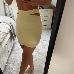 Gul kjol med cut-out detalj - Säljer en gul kjol med unik cut-out detalj i midjan. Kjolen är kort och har en tight passform som framhäver figuren. Endast använd en gång.