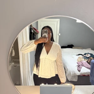 Vit v-ringad blus med struktur - Säljer en vit blus med v-ringning och lång ärm. Blusen har en strukturerad yta och markerad midja som ger en fin siluett. Perfekt att styla med jeans eller kjol för en trendig look.