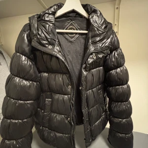Svart pufferjacka från Parajumpers - Säljer en svart pufferjacka med glansig finish. Jackan har lång ärm, dragkedja framtill och hög krage. Perfekt för kyliga dagar och riktigt snygg den ser helt ny jätte varm till vintern och kommer sälja den för bra pris och den ser ut som en moncler jacka.