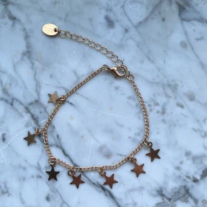 Guldfärgat armband med stjärnberlocker - Säljer ett fint armband i guldfärg med små stjärnberlocker. Kedjan är tunn och har justerbar längd med ett litet märke vid låset. Perfekt accessoar för att ge lite extra glans till din stil.