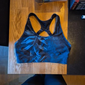 Sport-bh från OTP blå bladig - Sportbh från OTP i fint skick. Mörkblå med bladigt mönster.                          Bh:n har brottarrygg och justerbara axelband för extra stöd. Materialet är stretchigt och består av 80% polyester och 20% spandex.    Den är hel men har en tråd som sticker ut se bild 4. Storlek S 36/38 går det att utläsa även fast det va svårt att få på bild.