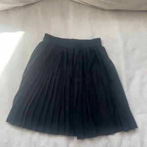 Svart plisserad kjol från NA-KD - Säljer en svart plisserad kjol från NA-KD i storlek XS. Kjolen har bred resår i midjan och är kort i modellen. Perfekt inför sommaren💕#NAKD