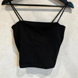 Svart croppad topp - Säljer en svart croppad linnetopp med smala axelband. Enkel och stilren design som passar perfekt till sommaren. Toppen har en rak skärning och är tillverkad i ett mjukt material.