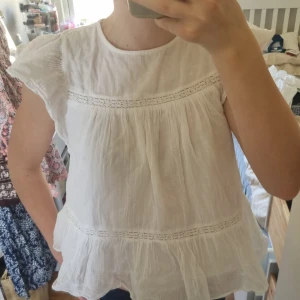 Vit blus med volang från Gina Tricot - Säljer en söt vit blus från Gina Tricot med volangdetaljer och korta ärmar. Blusen har rund halsringning, fina spetsinslag och en luftig, flowy passform. Perfekt för varma dagar och enkel att styla till olika outfits.Har användit några gånger men i nyskick.  Frakt ingår inte. Säljer för att jag har växt ur dem. 