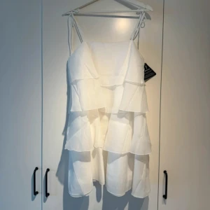 Vit volangklänning från Gina Tricot - Superfin vit klänning från Gina Tricot i organza med flera lager volanger och smala axelband. Perfekt för sommarens alla tillfällen när du vill känna dig extra söt och trendig.