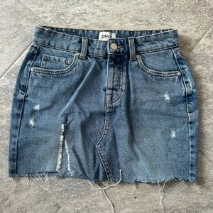 Kort jeanskjol från ONLY - Säljer en kort blå jeanskjol från ONLY då den har blivit för liten för mig .Toppen skick!🩷rå kant och har slits och slitningar framtill. 