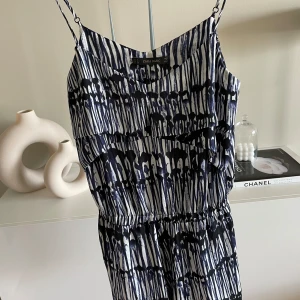 Mönstrade jumpsuit med resår från Zara. S - .•Snygg och elegant playsuit från Zara i ett iögonfallande blåvitt mönster.  •Jumpsuiten har tunna axelband och en figursydd design.  •Den har en dekorativ volangdetalj över bysten och en elastisk midja för en bekväm passform.  •Perfekt för både vardag och fest. •Använd en gång •Djur & rökfritt hem
