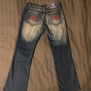 Victoria Beckham lågmidjade bootcut jeans - Säljer ett par blå jeansbyxor från Red & Republic med röda broderade kronor på bakfickorna.  Säljer då de är förstora för mig men de har mycket bra skick, inga skavanker. Måtten är:                                Midja rakt över: 38 cm Innerbenslängd: 71 cm Yttrebenslängd: 97 cm Lårbredd: ca 22