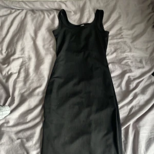 Svart ribbad klänning - En svart ribbad klänning med tight passform och ärmlös design. Klänningen har rundad halsringning och är tillverkad i ett stretchigt material som sitter snyggt på kroppen. Perfekt för dig som gillar en enkel och stilren look.